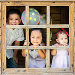 Three young children that are siblings smiling and looking out the window of a playhouse for psychology resources blog post that has helpful tips and content.