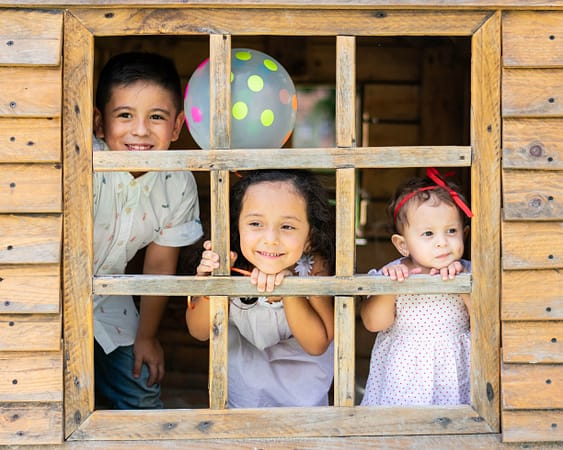 Three young children that are siblings smiling and looking out the window of a playhouse for psychology resources blog post that has helpful tips and content.